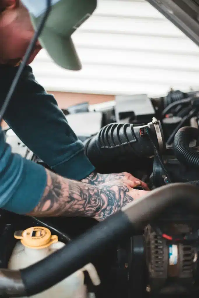 mécanicien effectuant un contrôle sous le capot lors d’un entretien auto pour garantir le bon fonctionnement du moteur. ​​